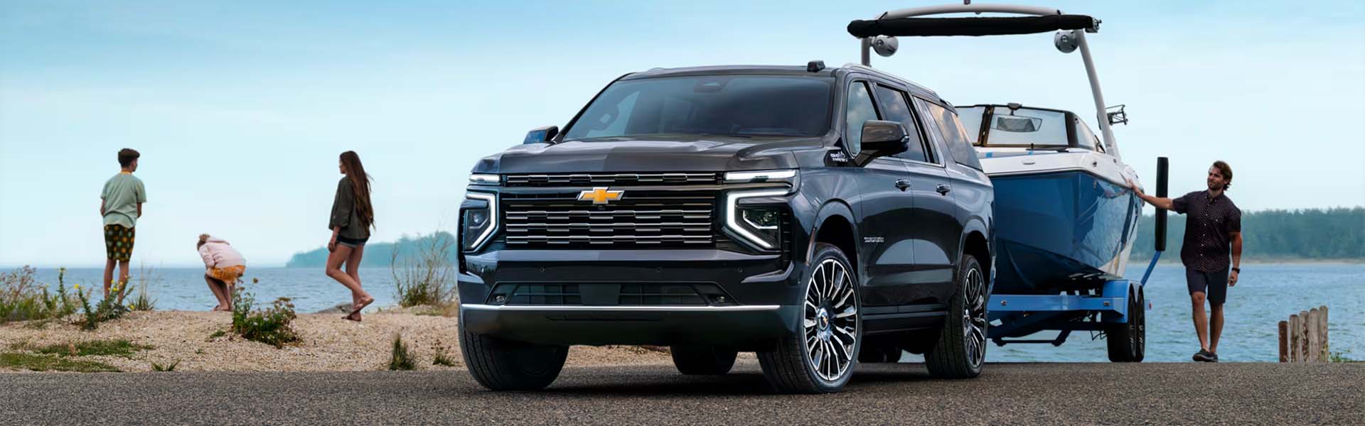 2025 Chevrolet Suburban towing a large blue boat at a lakeside, highlighting the vehicle’s powerful towing capacity, family-friendly design, and outdoor adventure capability.