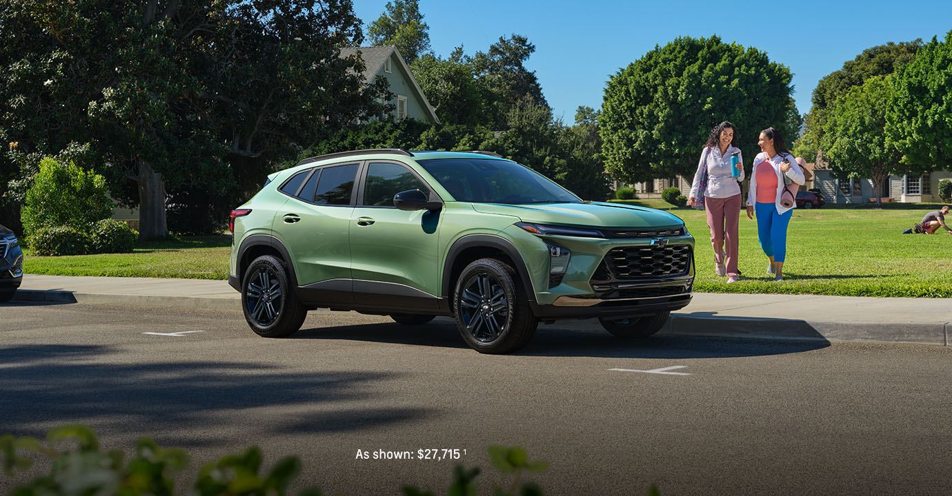 2026 Chevy Trax green compact SUV parked on a residential street with two women walking on the sidewalk nearby