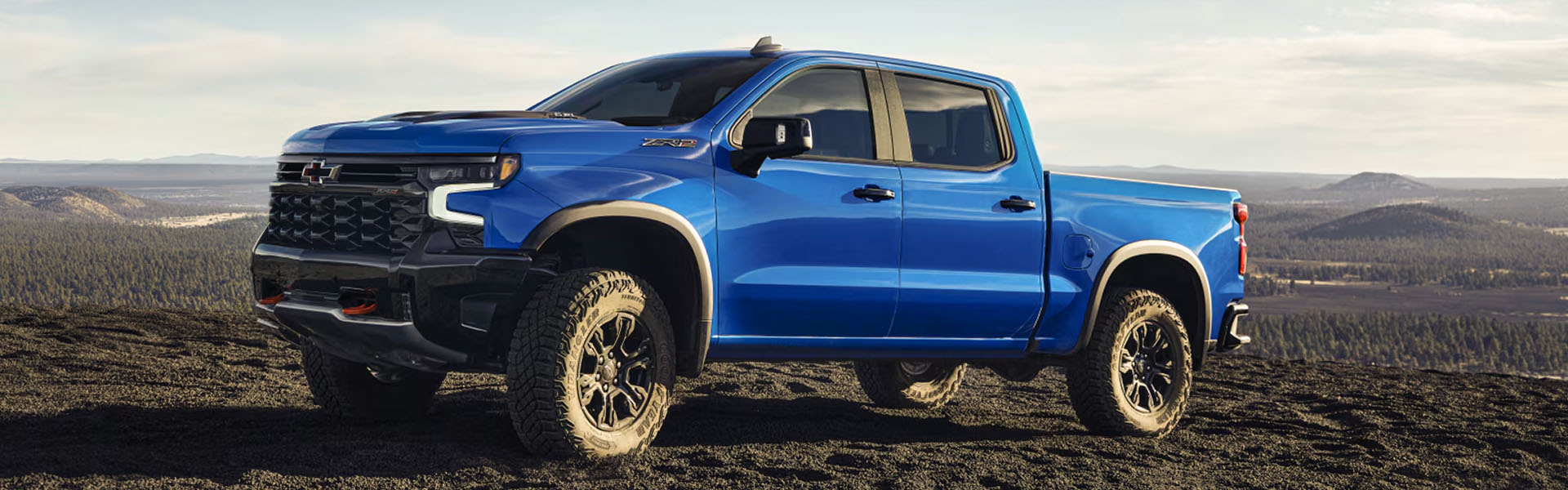 2026 Chevrolet Silverado 1500 in blue color parked on rocky terrain with mountains in the background.