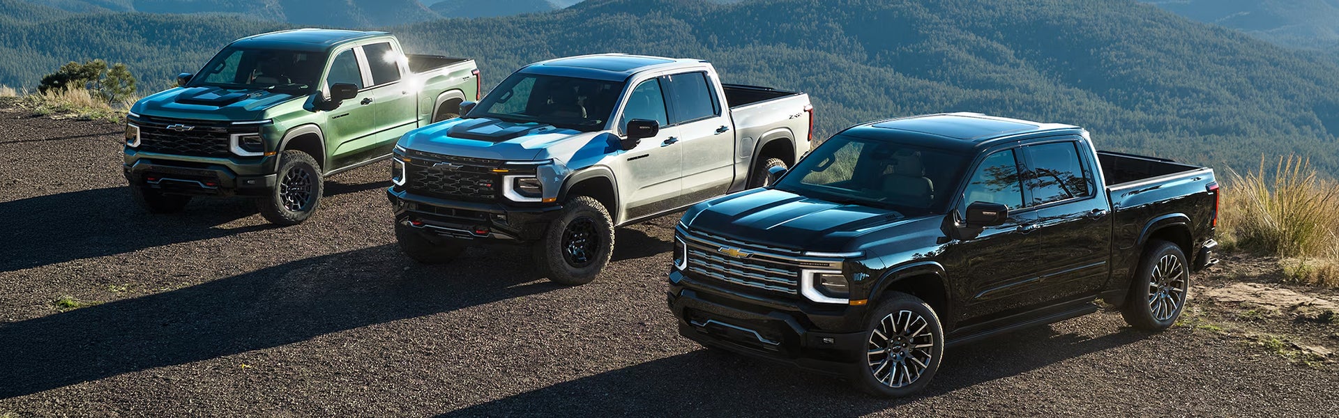 Three 2027 Chevrolet Silverado 1500 parked near mountain landscape showcasing its exterior features.